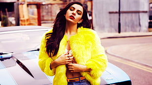 woman wearing yellow fur coat and blue denim bottoms standing beside black car HD wallpaper