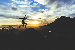 silhouette of man jumping over mountain during golden hour