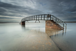 black and brown bridge in the middle of body of water under nimbostratus cloud