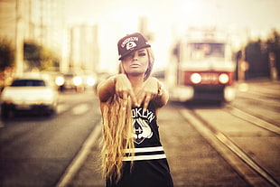 shallow focus photography of woman in black and white tank top and black and white snapback cap in middle of road with tram and cars HD wallpaper