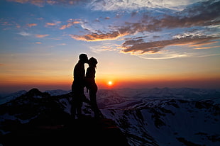 silhouette of man and woman kissing on mountain cliff HD wallpaper