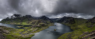 green grass covered mountains in between small body of water under clouded gray sky