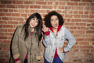 two women wearing jacket standing beside a concrete brick wall HD wallpaper