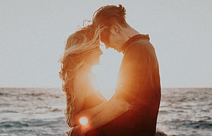 couple hugging near ocean during golden hour HD wallpaper