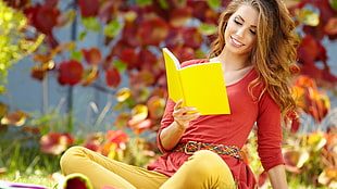 women in red elbow-sleeve top looking at yellow book