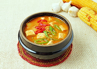 yellow soup with tofu,green and red peppers on black ceramic pot HD wallpaper