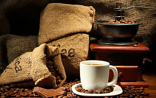 white ceramic cup and saucer set filled with coffee placed on brown wooden panel surround by lots of coffee beans