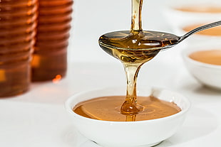 stainless steel spoon pouring of honey in round white ceramic bowl