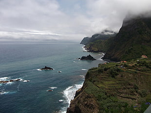 body of ocean near mountain hills under cloudy sky during daytime