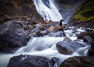 man standing on water falls rock with body of water photography during daytime