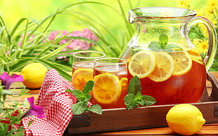 lemon ice tea in clear glass pitcher and two drinking glasses on brown wooden tray on table