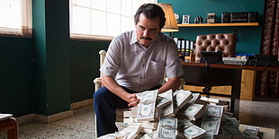 man wearing white button-up shirt sitting on white wooden armchair near pile of bundle of US dollar bills HD wallpaper