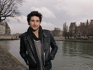 man wearing grey shirt and black leather jacket near body of water during daytime HD wallpaper