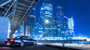 black car beside lighted high-rise buildings