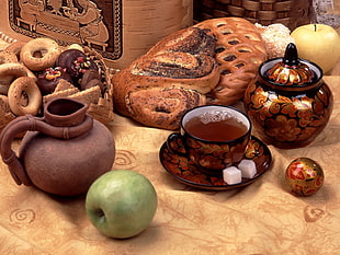 green Apple fruit near brown and black ceramic tea cup filled with tea with 2 white sugar cubes beside bread