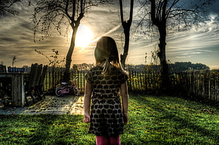 girl wearing black short sleeve dress with pink pants standing on green grass field