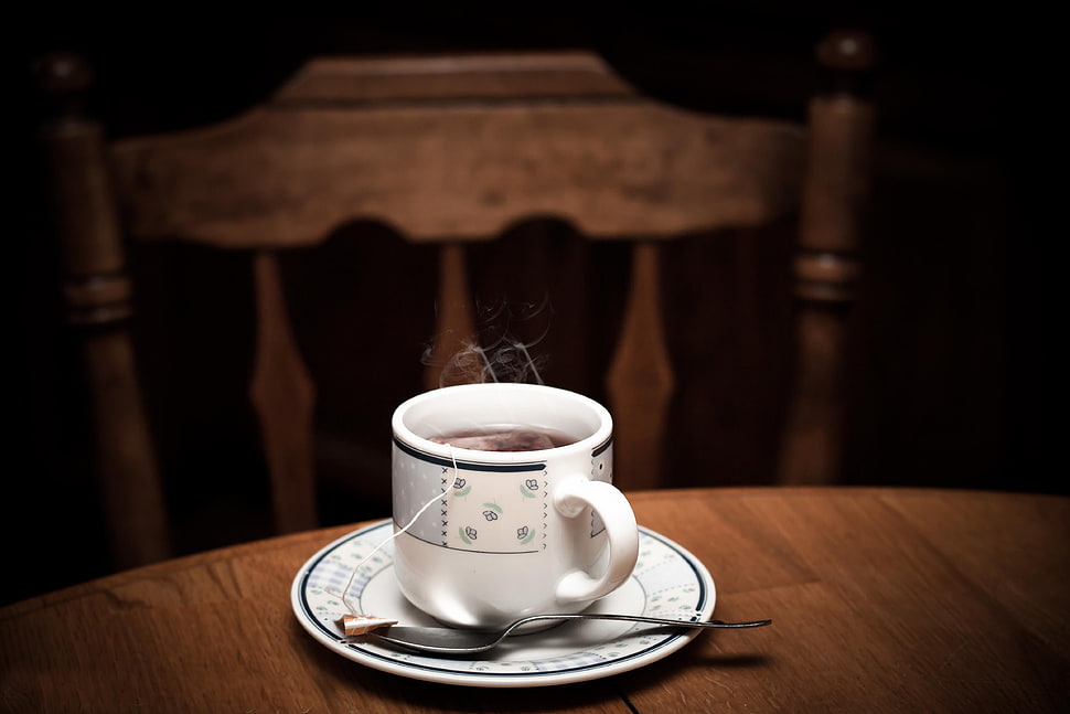 white-and-black floral print teacup and saucer filled with black coffee on brown wooden table near brown wooden bannister chair HD wallpaper