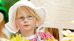 girl in white hat and eyeglasses standing behind yellow flowers during daytime