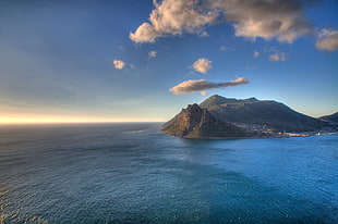 aerial view of a mountain surrounded by water under a blue cloudy sky