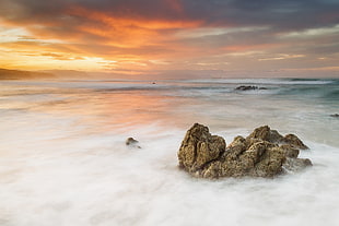 body of water covered with fog during sunset