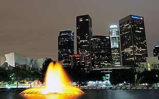 timelapse photo of a fountain near skyscrapers during nighttime HD wallpaper