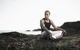 man in black tank top sitting on gray rocky shore HD wallpaper
