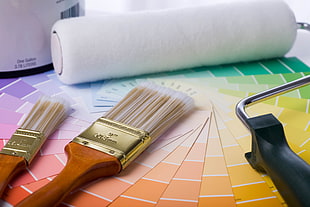 two brown wooden handle paint brushes beside white paint roller