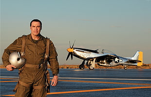 male pilot holding gray helmet with biplane background during daytime