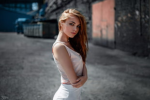 blonde-hair woman wearing white sleeveless top with hand on elbow facing sidewards