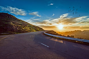 gray concrete road near brown rock cliff with sunset as a background