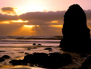 silhouette of rock fragment on beach seashore during sunset