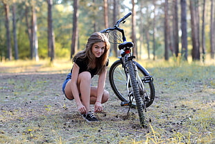 woman in black shirt and blue short shorts sitting beside bicycle HD wallpaper