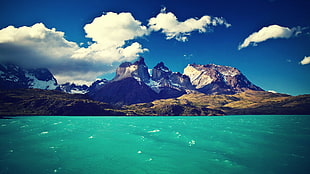 body of water near mountains under cloudy sky