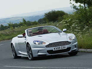 timelapse photo of man in gray Bentley convertible coupe on black concrete roa