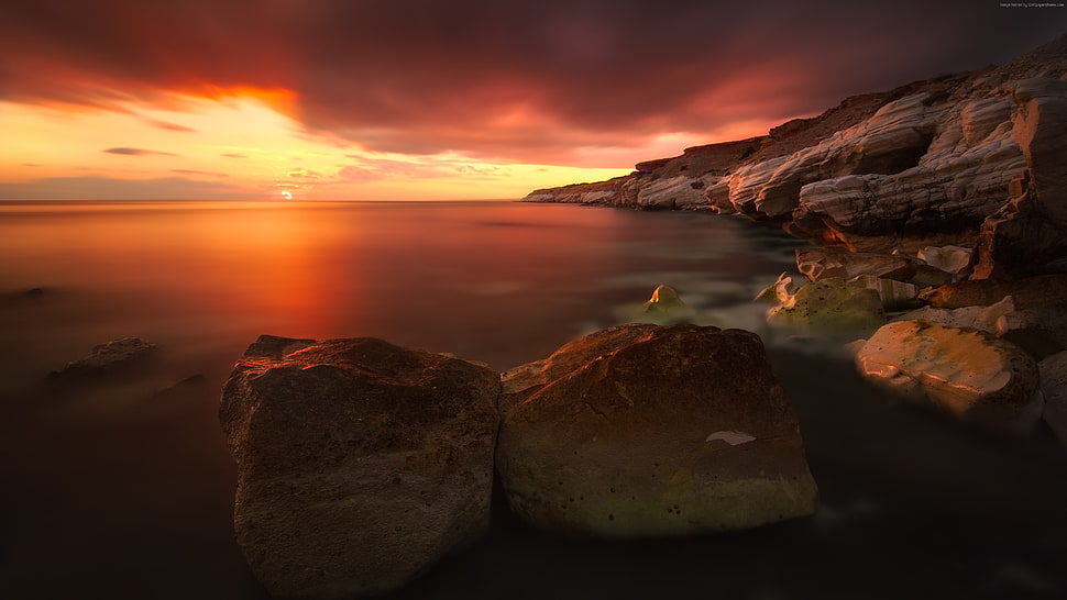 calm body of water near cliff during golden hour HD wallpaper