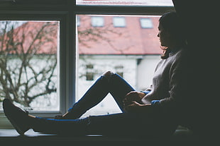 woman sitting and leaning on concrete wall near frame glass window