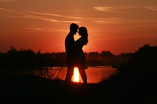 silhouette of couple standing near calm lake HD wallpaper