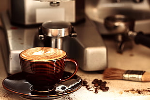 cup of cappuccino beside coffee grinder with brush near portafilter