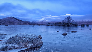 landscape photography of mountain range in front of body of water during snow season