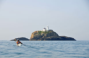 man riding boat on body of water near lighthouse during daytime HD wallpaper