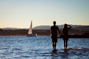 woman and man standing on rock formation surrounded by water near sail ship