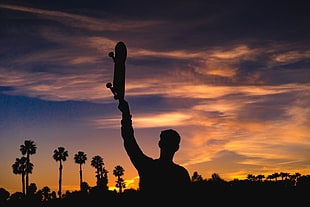 silhouette of man raising skateboard during golden hour time HD wallpaper