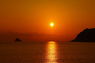 mountain beside ocean under sunset