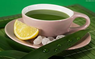 white ceramic coffee mug filled with green liquid with slice of lemon on banana leaf