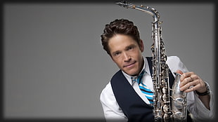 man in white dress shirt with black waistcoat holding grey saxophone