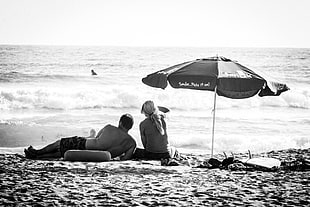 grayscale photo of couple sitting under umbrella near body of water HD wallpaper
