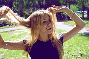 blonde haired woman in blue t-shirt raising her hands holding her hairs smiling