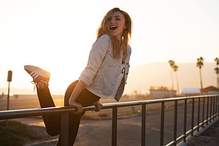 woman wearing white denim jacket holding metal rails smiling during golden hour HD wallpaper