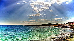 sun rays through clouds reflecting on rippling body of water during daytime