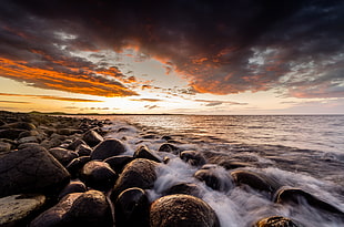 rocks on seashore under gray clouds during sunset HD wallpaper